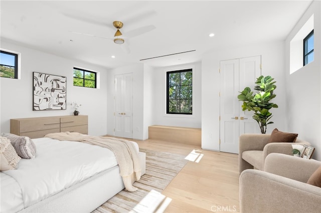 bedroom featuring recessed lighting, ceiling fan, light wood finished floors, and two closets