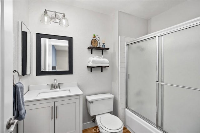 bathroom with toilet, baseboards, combined bath / shower with glass door, and vanity