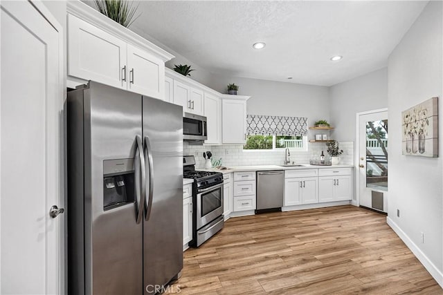 kitchen with light wood finished floors, decorative backsplash, stainless steel appliances, light countertops, and white cabinetry