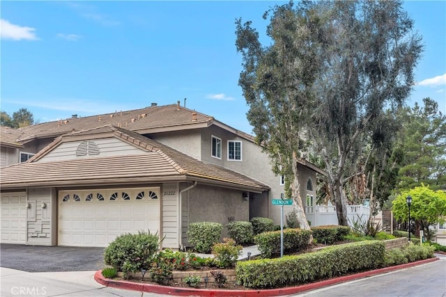 view of front of property featuring driveway, a garage, a tile roof, fence, and stucco siding