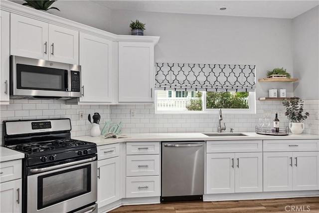 kitchen featuring white cabinets, wood finished floors, stainless steel appliances, light countertops, and a sink