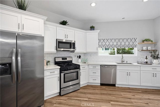 kitchen featuring tasteful backsplash, white cabinets, stainless steel appliances, light countertops, and a sink