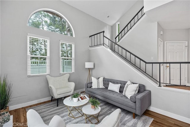 living area with high vaulted ceiling, baseboards, stairway, and wood finished floors