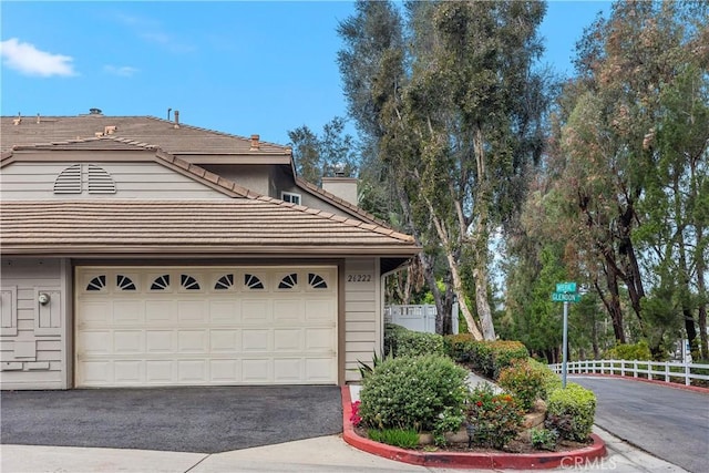 view of home's exterior featuring aphalt driveway, a tile roof, a chimney, fence, and a garage