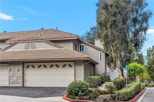 view of front of house featuring an attached garage, a tile roof, fence, driveway, and stucco siding