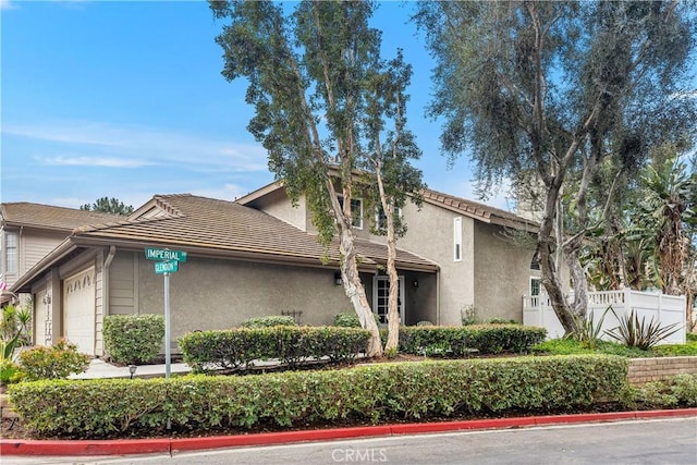 exterior space with a tile roof, fence, an attached garage, and stucco siding