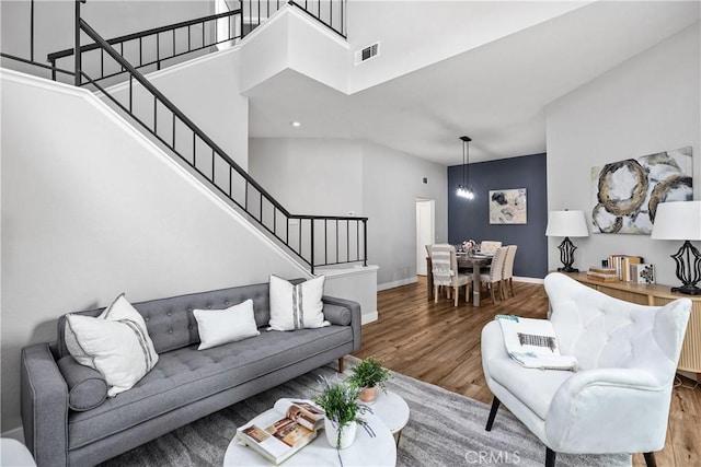 living room with a high ceiling, wood finished floors, visible vents, baseboards, and stairs