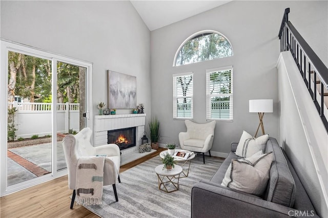 living room with high vaulted ceiling, wood finished floors, baseboards, stairs, and a brick fireplace