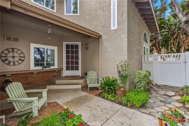 view of exterior entry featuring a patio area, fence, a gate, and stucco siding