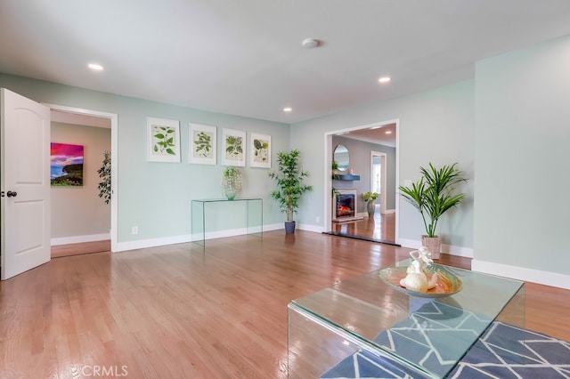 interior space featuring a warm lit fireplace, recessed lighting, wood finished floors, and baseboards