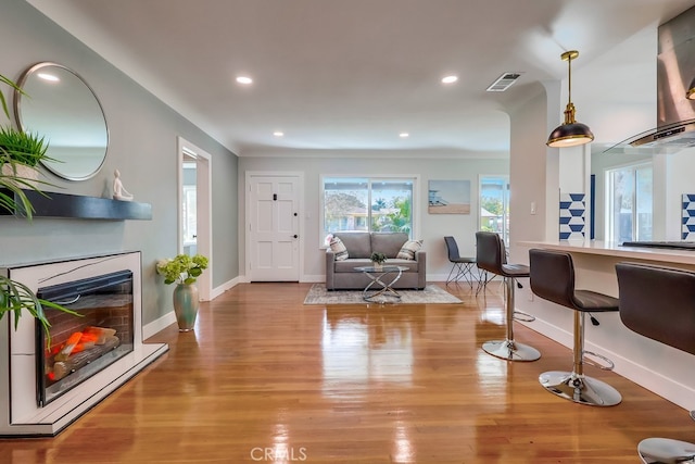 living area with visible vents, baseboards, a glass covered fireplace, light wood-style flooring, and recessed lighting