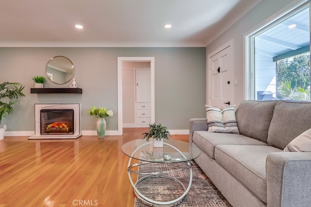 living room featuring a glass covered fireplace, recessed lighting, baseboards, and wood finished floors