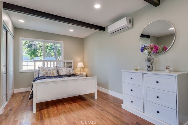 bedroom featuring light wood finished floors, beam ceiling, baseboards, and an AC wall unit