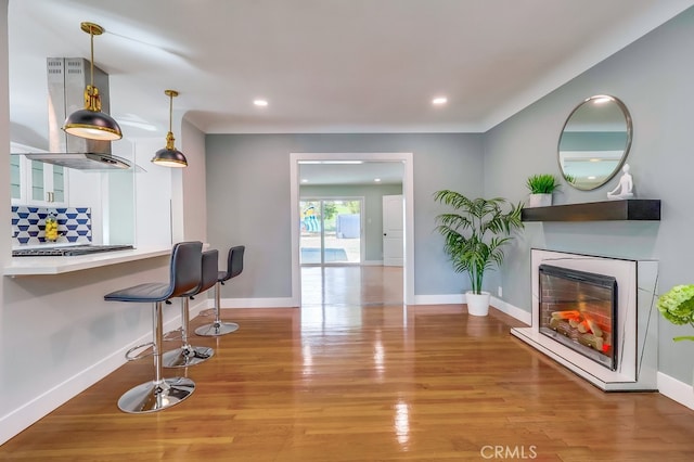 interior space with a warm lit fireplace, baseboards, wood finished floors, and recessed lighting