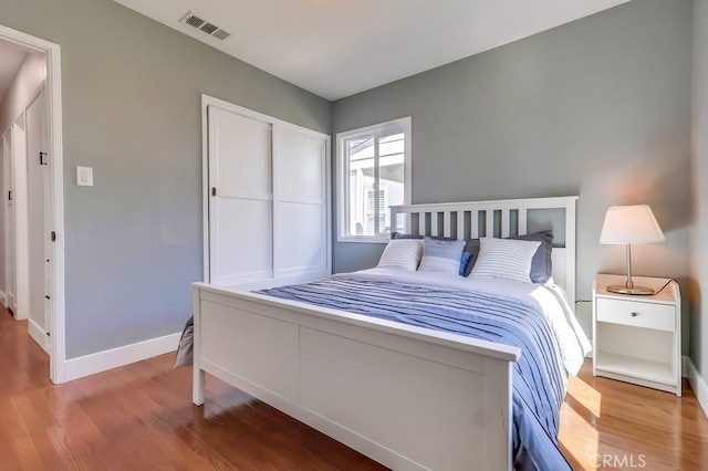 bedroom featuring baseboards, a closet, visible vents, and wood finished floors