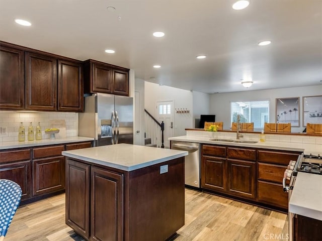 kitchen with stainless steel appliances, light countertops, light wood-style floors, a sink, and a kitchen island