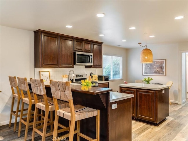 kitchen with tasteful backsplash, appliances with stainless steel finishes, a center island, dark brown cabinets, and light wood-type flooring