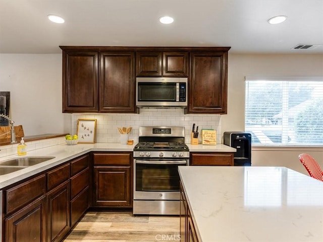 kitchen with light wood finished floors, tasteful backsplash, visible vents, stainless steel appliances, and a sink