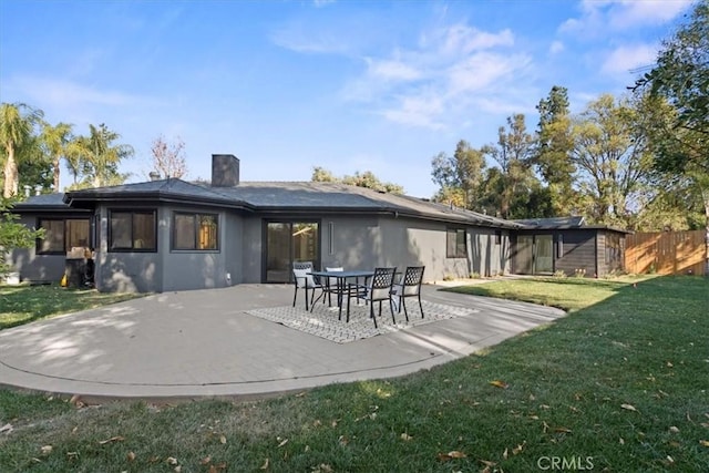 rear view of house with a patio area, a chimney, stucco siding, and a yard