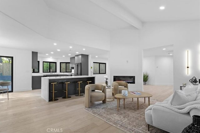 living area with a glass covered fireplace, beam ceiling, light wood finished floors, and recessed lighting