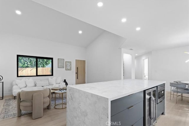 kitchen with light wood finished floors, a kitchen island, wine cooler, light stone counters, and gray cabinets