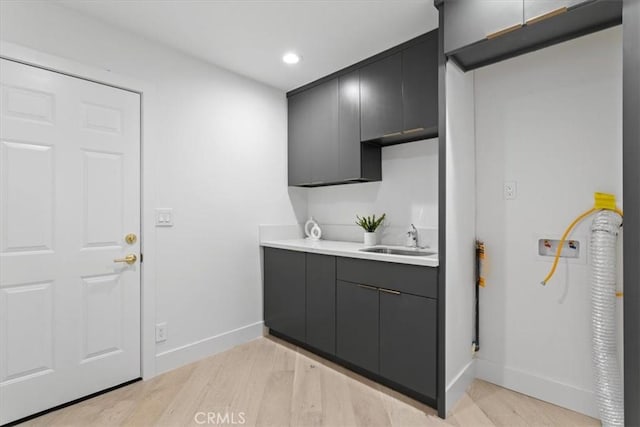 kitchen featuring baseboards, light countertops, a sink, and light wood finished floors