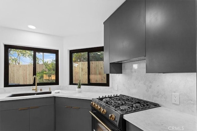 kitchen featuring stainless steel gas stove, gray cabinets, a sink, and light countertops