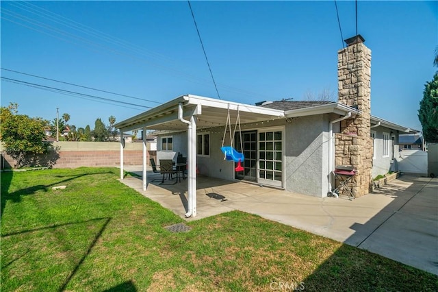 rear view of house featuring a lawn, a patio, a fenced backyard, a chimney, and stucco siding