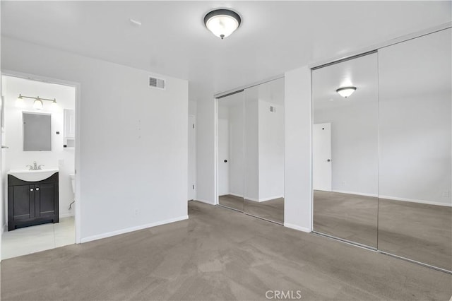 unfurnished bedroom with light carpet, visible vents, connected bathroom, multiple closets, and a sink