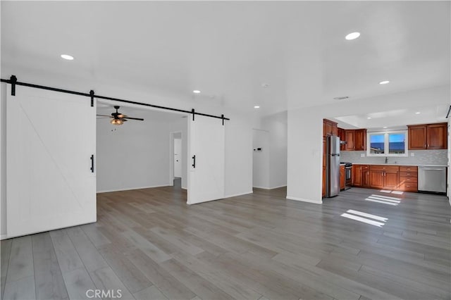 unfurnished living room with light wood finished floors, a barn door, and a sink