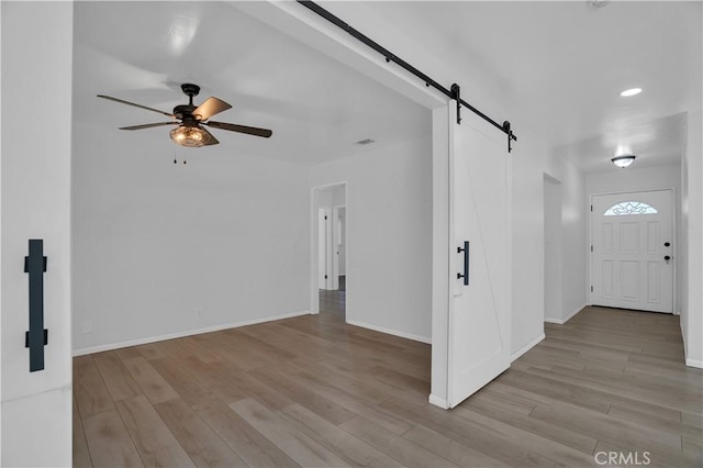 entryway featuring visible vents, a barn door, a ceiling fan, wood finished floors, and baseboards