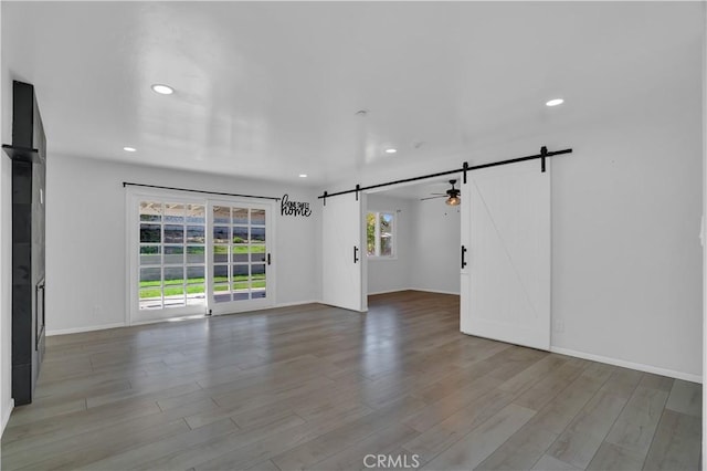 spare room with a barn door, baseboards, wood finished floors, and recessed lighting