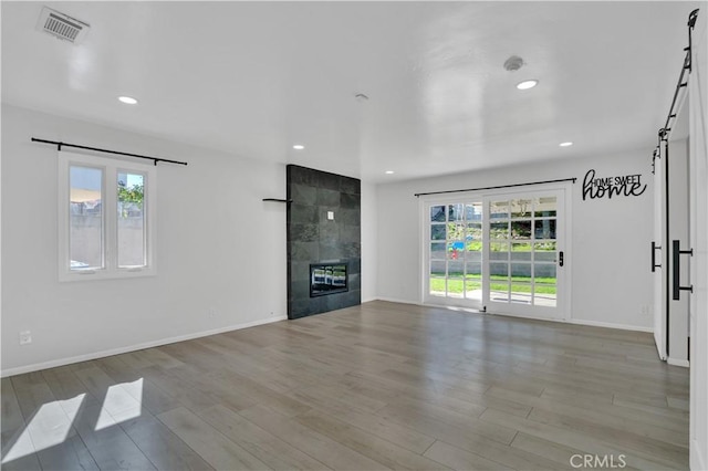 unfurnished living room featuring a barn door, visible vents, wood finished floors, and a tile fireplace