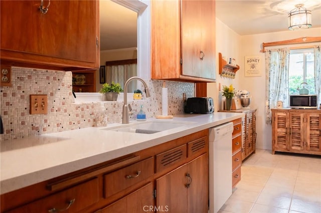 kitchen featuring brown cabinets, light countertops, decorative backsplash, a sink, and dishwasher