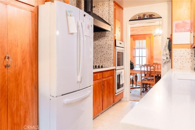 kitchen featuring brown cabinetry, white appliances, light countertops, and wall chimney exhaust hood