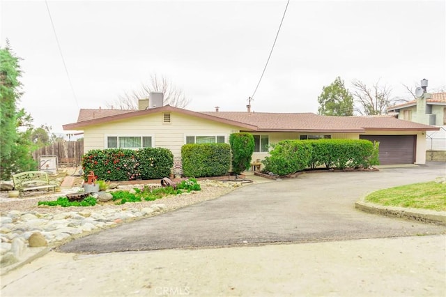 ranch-style home with aphalt driveway, a chimney, an attached garage, and fence