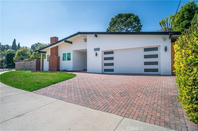 view of front of home with a garage, a chimney, decorative driveway, a front lawn, and stucco siding