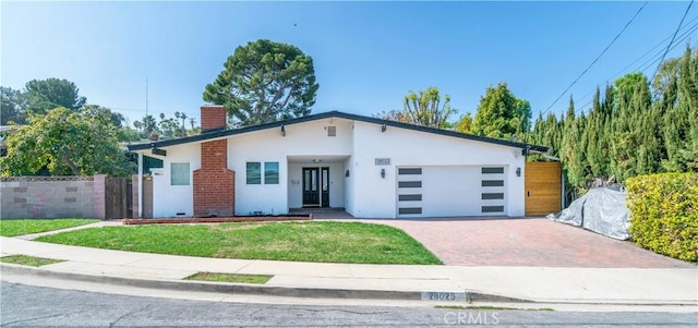 view of front of property with stucco siding, an attached garage, fence, decorative driveway, and a front yard