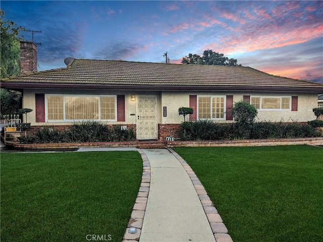 ranch-style home featuring brick siding, a chimney, a front lawn, and stucco siding