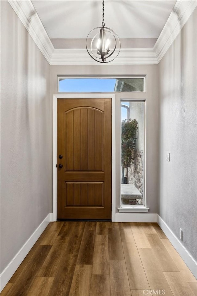 foyer featuring an inviting chandelier, baseboards, ornamental molding, and wood finished floors