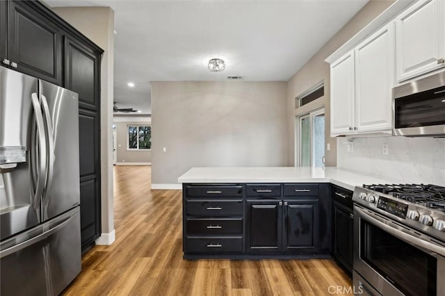 kitchen with light countertops, appliances with stainless steel finishes, white cabinetry, light wood-type flooring, and a peninsula