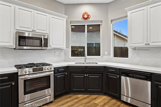 kitchen with stainless steel appliances, dark cabinetry, a sink, and white cabinetry