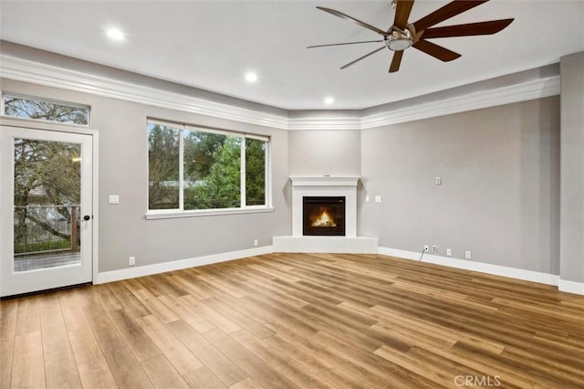 unfurnished living room with recessed lighting, ornamental molding, a glass covered fireplace, light wood-type flooring, and baseboards