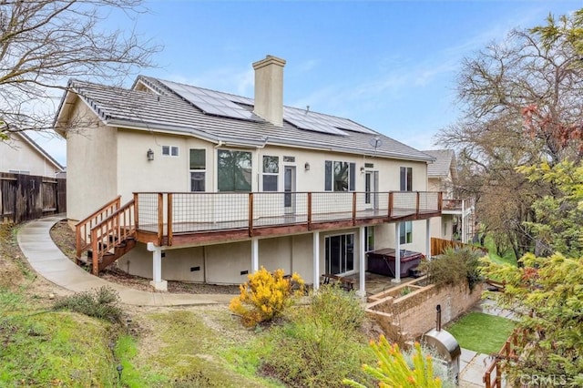 back of house with stucco siding, roof mounted solar panels, a chimney, and a wooden deck