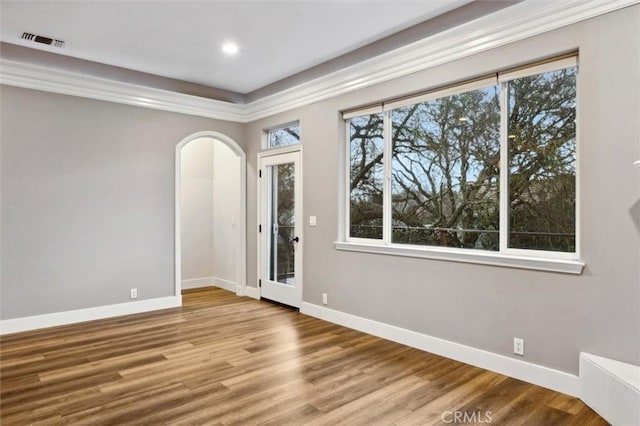 empty room with arched walkways, visible vents, baseboards, and wood finished floors