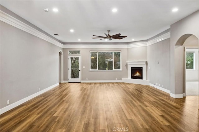 unfurnished living room with a warm lit fireplace, arched walkways, and wood finished floors