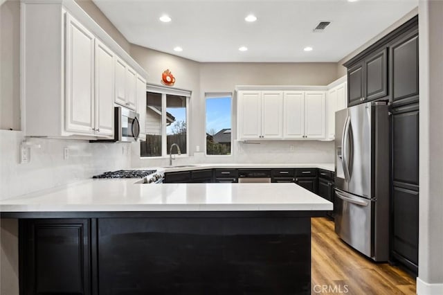 kitchen with visible vents, a peninsula, stainless steel appliances, light countertops, and a sink