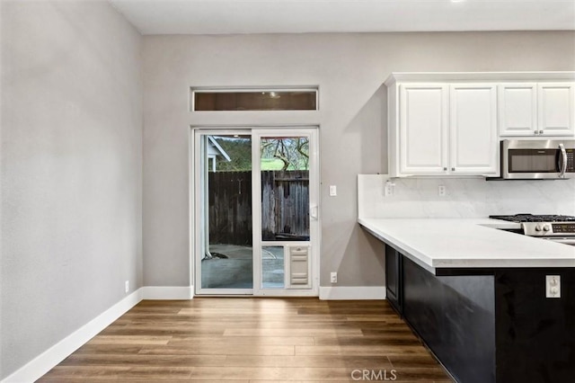 kitchen featuring baseboards, stainless steel microwave, wood finished floors, and white cabinets