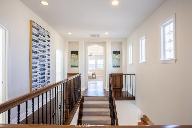 corridor with visible vents, arched walkways, baseboards, an upstairs landing, and recessed lighting