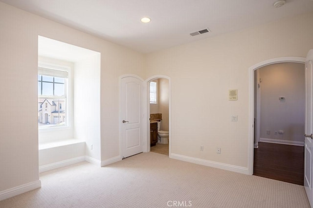 unfurnished bedroom featuring arched walkways, multiple windows, visible vents, and light colored carpet